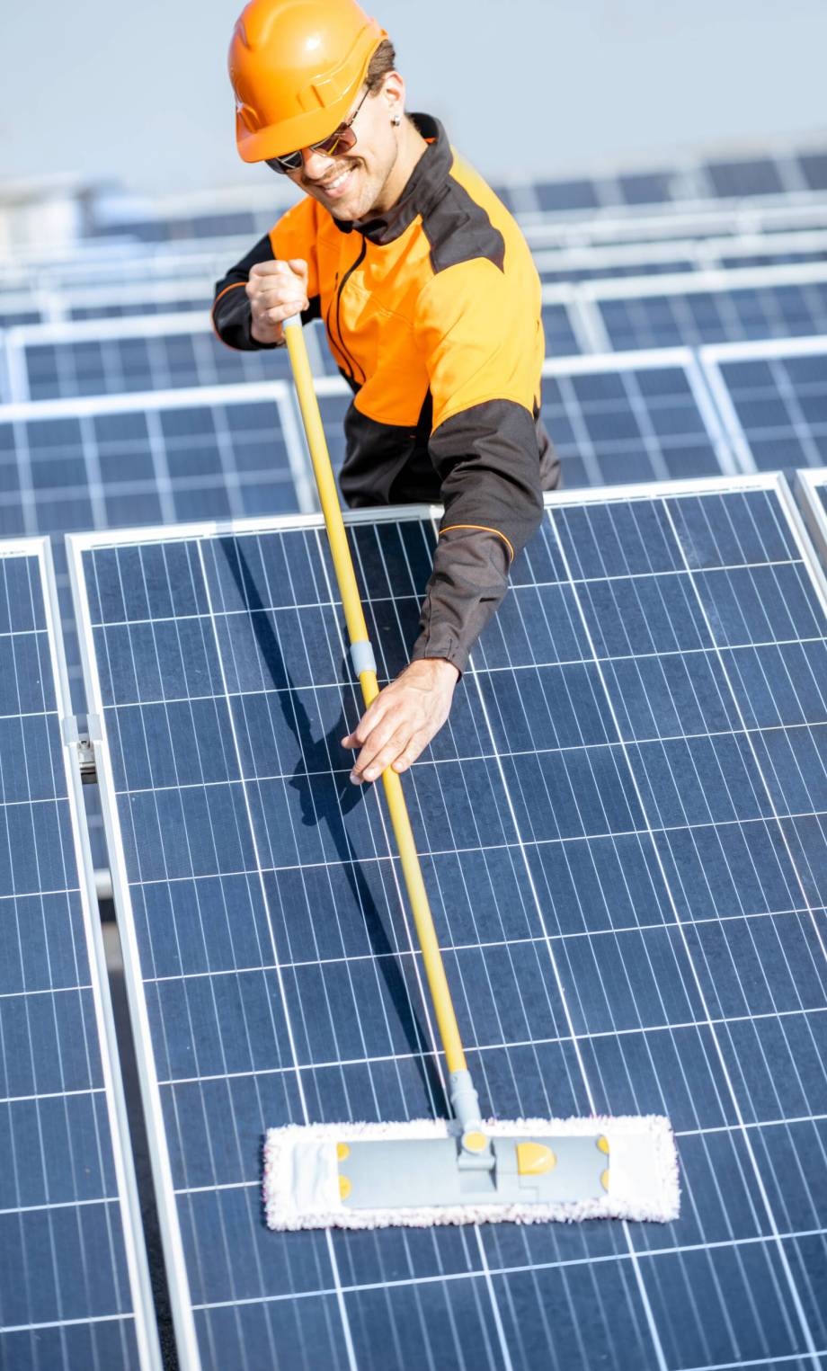 Professional cleaner in protective workwear cleaning solar panels with a mob. Concept of solar power plant cleaning service